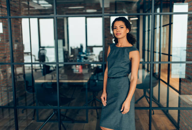 Kobieta w profesjonalnej sukni pewnie stoi w nowoczesnym biurze.