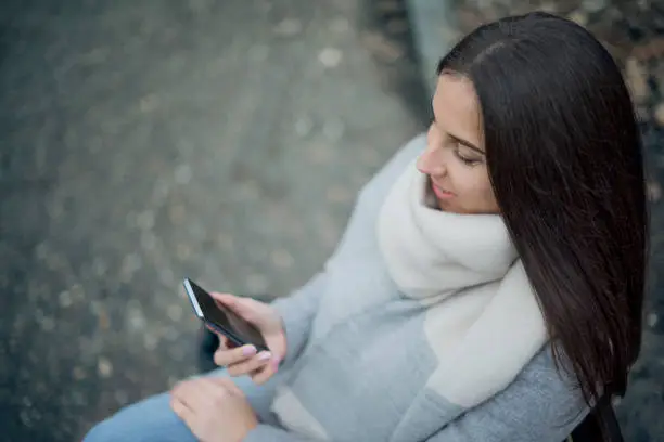 Woman sitting on bench and holding cellphone. Close up.