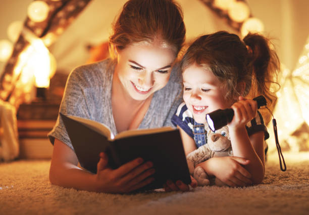 istock mother and child daughter reading a book and a flashlight before going to bed 939838184