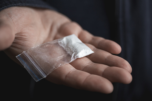 Mans hand holding on palm plastic packet with cocaine powder or another drugs. Drug dealer proposes to try narcotic concept, selective focus