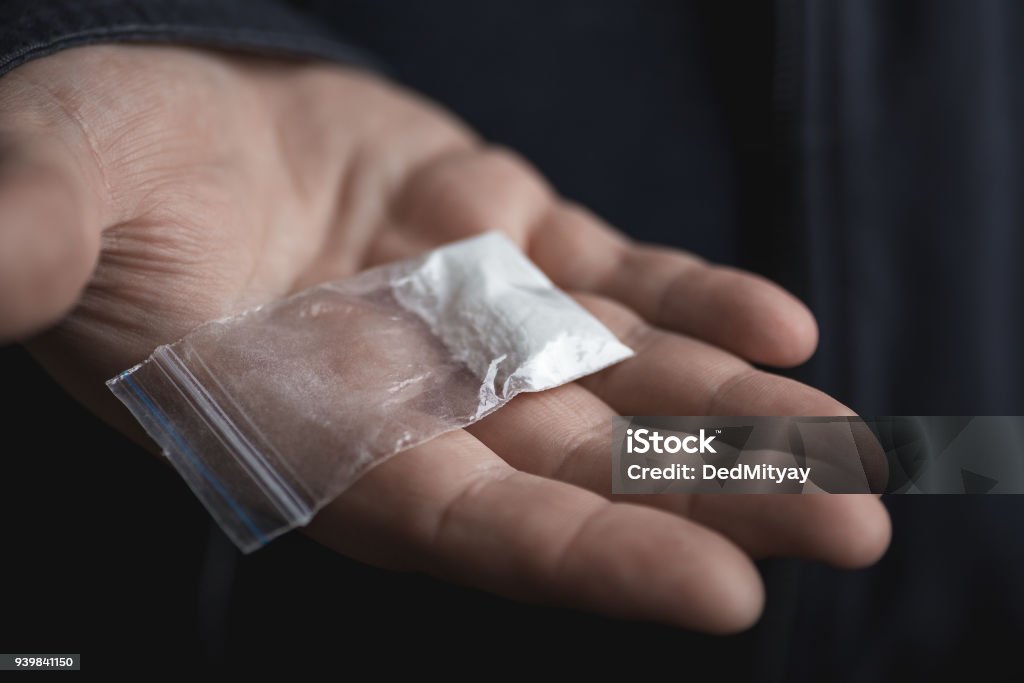 Mans hand holding on palm plastic packet with cocaine powder or another drugs. Drug dealer proposes to try narcotic concept Mans hand holding on palm plastic packet with cocaine powder or another drugs. Drug dealer proposes to try narcotic concept, selective focus Cocaine Stock Photo