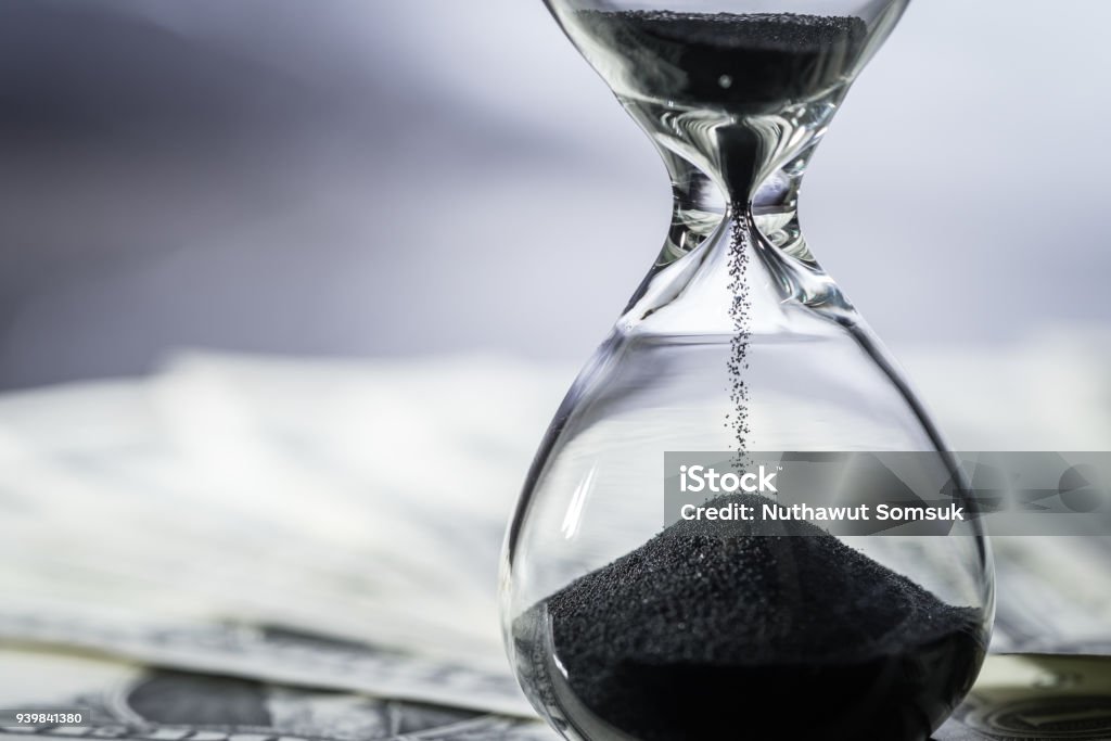 Closed up of sand falling in sandglass or hourglass on US Dollar bills as time running, long term investment or financial deadline concept Closed up of sand falling in sandglass or hourglass on US Dollar bills as time running, long term investment or financial deadline concept. Time Stock Photo