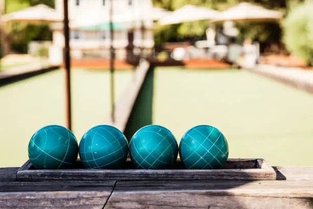 Teal colored Bocce Balls lined up ready to play a game with green lane blurred in background at a resort setting.