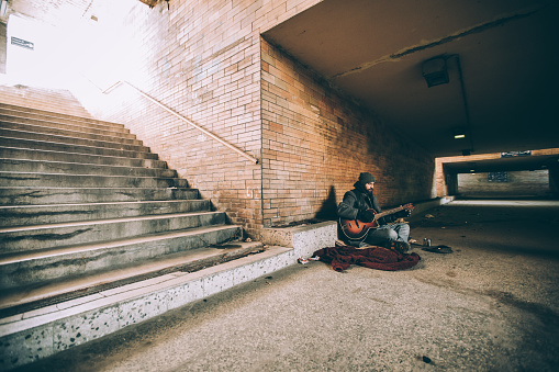 One man, young homeless man playing acoustic guitar on the street and begging.