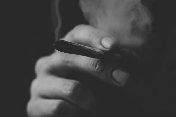 istock Smoke on a black background. A man smokes cannabis weed, a joint and a lighter in his hands. Concepts of medical marijuana use and legalization of the cannabis.Black and white 939862600