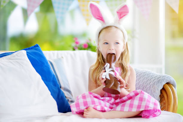 istock Cute little girl wearing bunny ears eating chocolate Easter rabbit 939870934