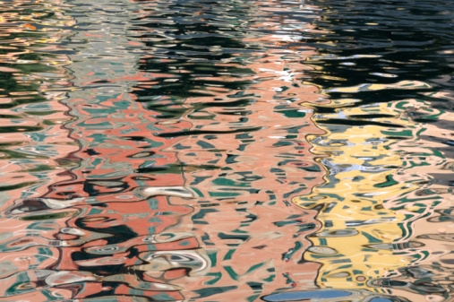 This horizontal color photograph is of the water's reflection in Vernazza, Italy. This is the third town in the National Park, Cinque Terre. In this abstract, travel background the colorful buildings are distorted by the surface of the rippling water.
