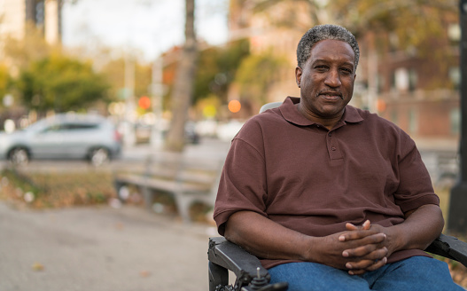 Portrait of the positive, optimistic disabled Black man, paralyzed veteran who sitting in wheelchair. Outdoor scene at the street in Bronx, New York City, USA