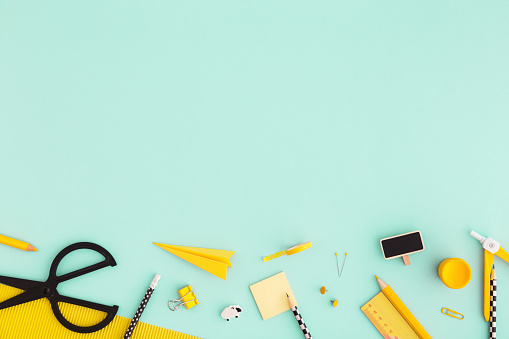 Creative, fashionable, minimal, school background with yellow supplies on cyan blue background. Back to school. Flat lay.