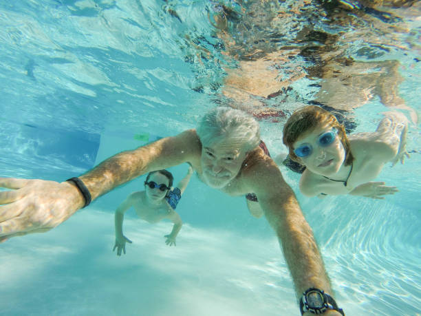 kinder, vater und großvater schwimmen unter wasser - active seniors retirement enjoyment swimming pool stock-fotos und bilder