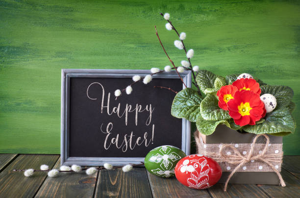 istock Easter basket with painted Easter eggs and red primrose pot flower on rustic wooden background, text 939892174