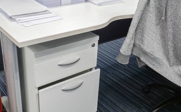 close up desk drawer and office desk with jacket on chair stock photo