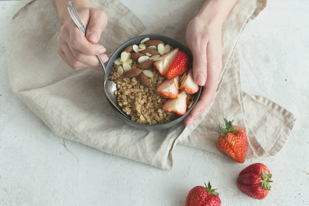 petit-déjeuner sain. bol en céramique gris avec granola, fraises et noix dans les mains de la femme. concept d’aliments diététiques et végétariens - cereal breakfast granola healthy eating photos et images de collection