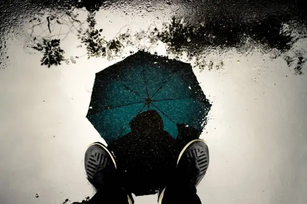 Photo of Reflection shadow man and umbrella walking in the rain.