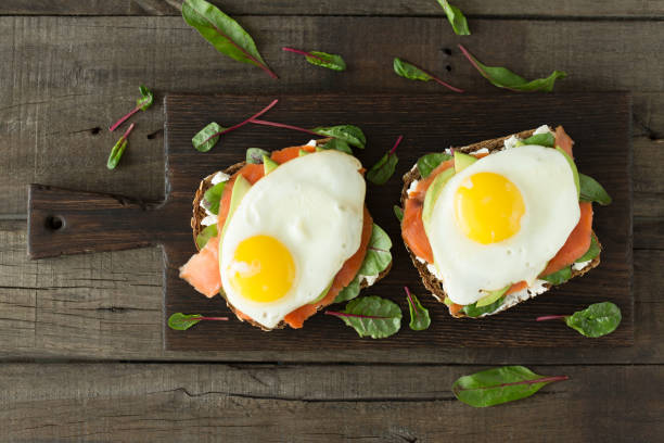 istock Healthy breakfast. Bread toasts with cheese, fried eggs, fish and fresh vegetables over wooden background, top view. Diet, weight loss food concept 939912100