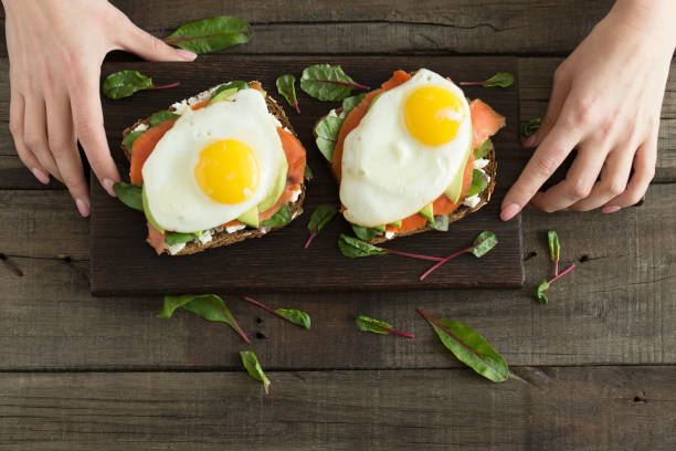 istock Healthy breakfast. Bread toasts with cheese, fried eggs, fish and fresh vegetables over wooden background, top view. Diet, weight loss food concept 939912146