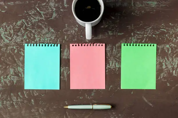 3 color blank sheets of mock-up, a cup of coffee, spoon and handle, on table texture dark. Top view. Copy space