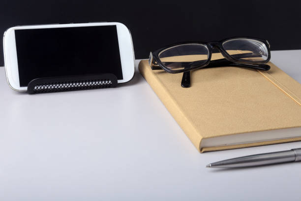 istock Modern white office desk table with laptop, smartphone and other supplies. Blank notebook page for input the text in the middle. Top view 939931748
