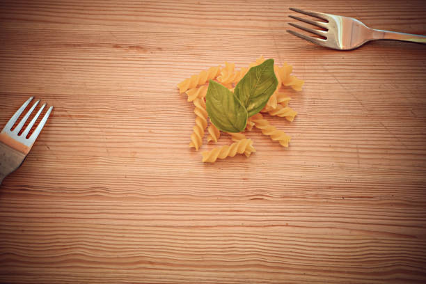 Raw pasta, forks and fresh basil at wooden background/ conceptual image of dieting