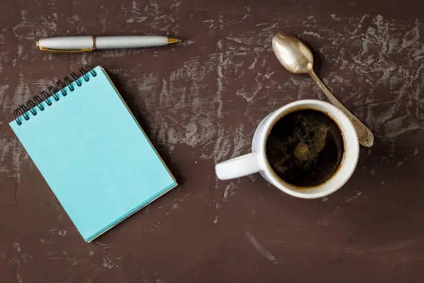 Notes mock-up, a cup of coffee, spoon and handle, on table texture darkly. Top view. Copy space