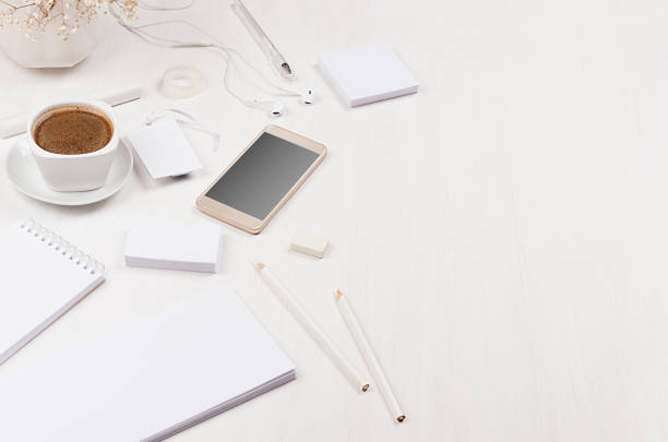 istock Elegant gentle soft white working place with white stationery, border, phone, coffee on white wooden board, closeup. 939958442