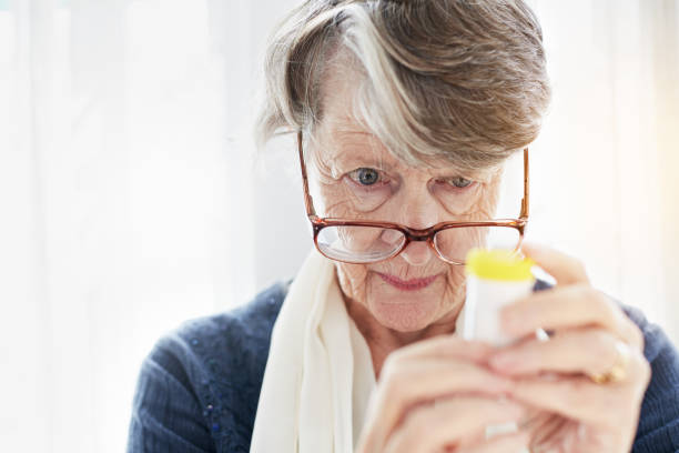 Old woman peers over spectacles checking label on medication