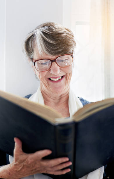 istock Smiling old woman looks down at book she holds 939978948