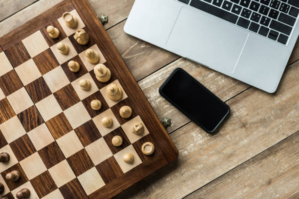 istock Smartphone, laptop and chess board with chess pieces on wooden surface 939987520