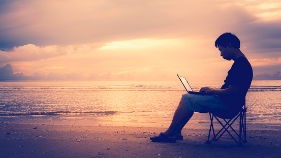 A man using laptop on the beach. Freedom with mobile technology concept.