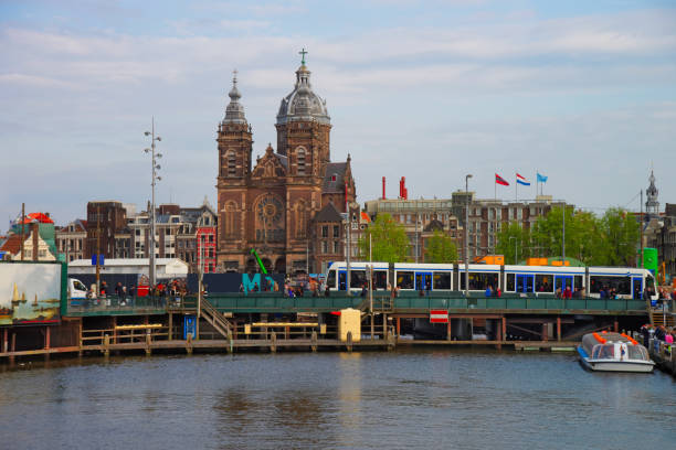 Amsterdam, Netherlands - May 2, 2013: Canal boats and St Nicholas Church in Open Havenfront, Amsterdam, Netherlands. People on the background