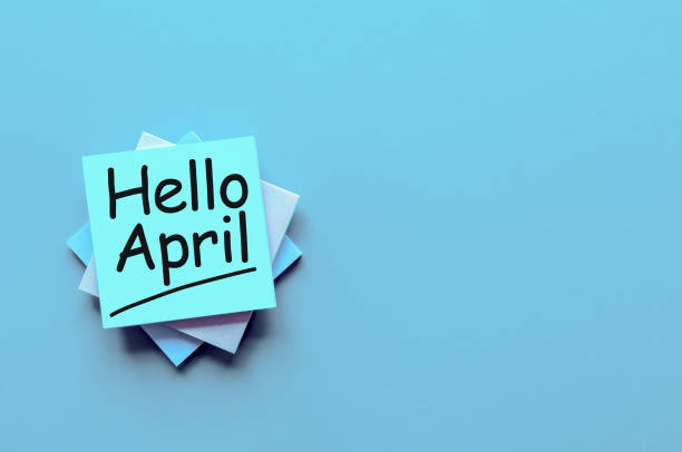 istock Hello April greeting written on blue paper stack at desk with empty space for text, mockup or template 940023354
