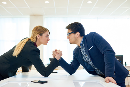 Serious confident business competitors participating in arm wrestling to prove leadership in honest fight in office