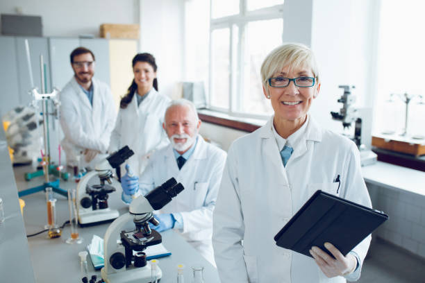 smiling senior scientist with her colleagues in laboratory - laboratory doctor white collar worker research imagens e fotografias de stock