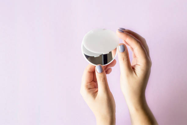 istock A compact, compact mirror in women's hands. On a lilac bright background. Makeup female accessories 940027684