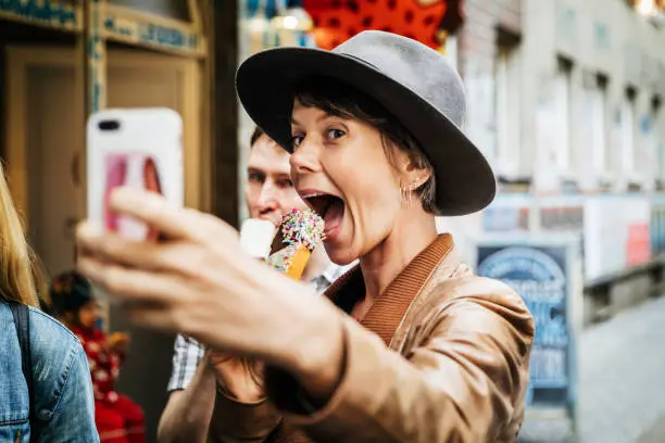 A tourist taking a selfie while eating an ice cream and grinning excitedly.