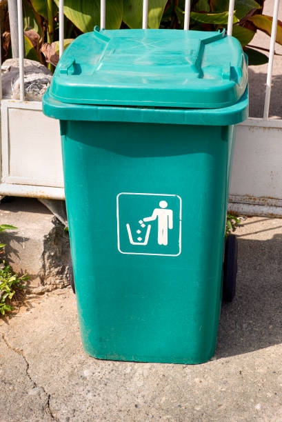 istock Green garbage can stands in front of fence. 940038542