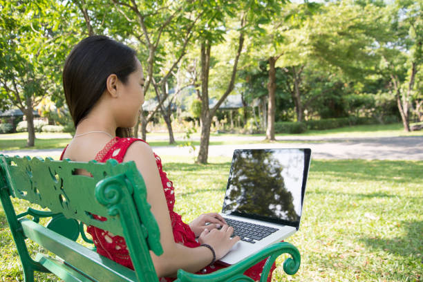 istock Asian woman using laptop on city park bench. 940046224