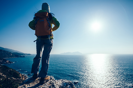 Successful female hiker standing on sunrise seaside mountain cliff edge