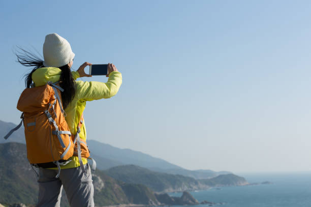 istock Young Woman Hiker Using Smartphone taking photo at Seaside 940049896