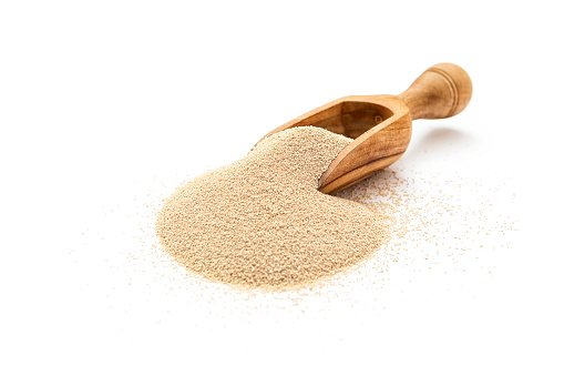 Dry yeast in wooden scoop on white background