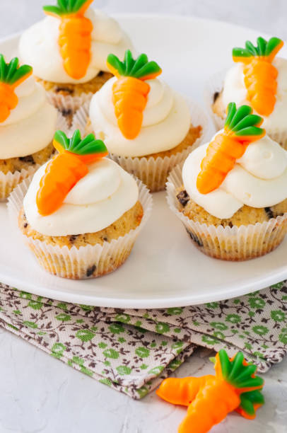 istock Vanilla cupcakes with chocolate chips and cream cheese frosting decorated with carrot marmalade in a plate on a white stone background. 940070042