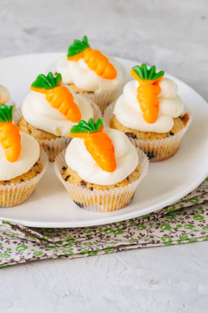 istock Vanilla cupcakes with chocolate chips and cream cheese frosting decorated with carrot marmalade in a plate on a white stone background. 940070046