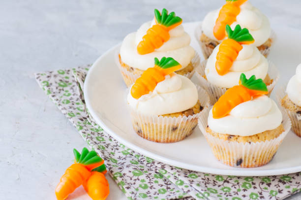 istock Vanilla cupcakes with chocolate chips and cream cheese frosting decorated with carrot marmalade in a plate on a white stone background. 940070048