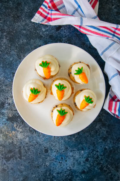 istock Vanilla cupcakes with chocolate chips and cream cheese frosting decorated with carrot marmalade in a plate on a blue stone background. 940070118