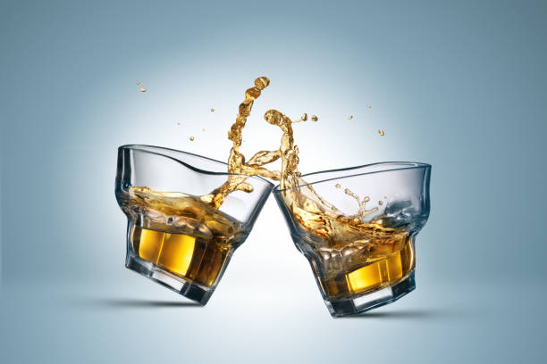 merging alcohol. two whiskey glasses clinking together on blue - action alcohol alcoholism bar imagens e fotografias de stock