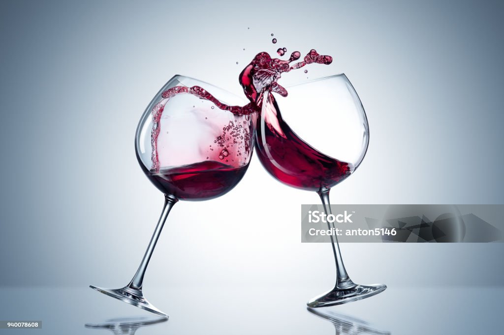 Two wine glasses in toasting gesture with big splashing. Alcohol concept. Two glasses of wine on the gray background Two wine glasses in toasting gesture with big splashing. Alcohol concept. Two glasses of wine on the gray background. Two transparent glasses. Trendy color. Merging alcohol Wine Stock Photo