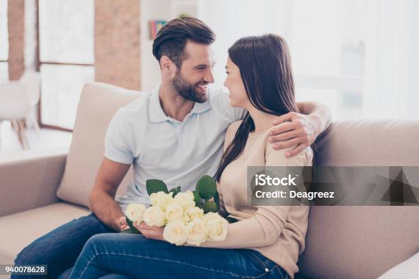 Viel Spaß Zusammen Mann Umarmt Seine Freundin Mit Rosen In Händen Sie Sind Zu Hause Auf Sofa Stockfoto und mehr Bilder von Beide Elternteile