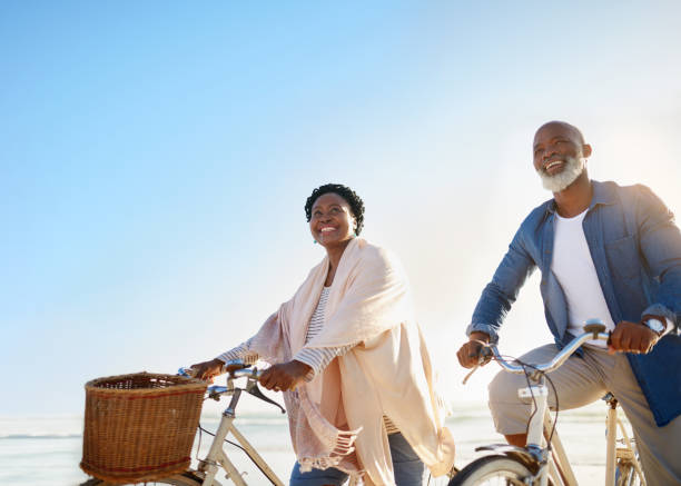 la retraite est une chance de profiter de nombreuses aventures plus - senior couple cycling beach bicycle photos et images de collection
