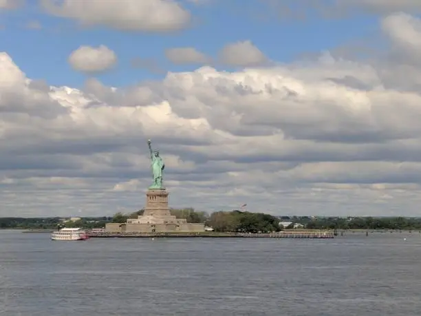 A view of the entire Statue of Liberty in New York, USA with water in the foreground and clouds in the background