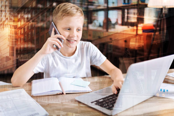 istock Smiling boy talking on the phone while looking at the laptop 940123366